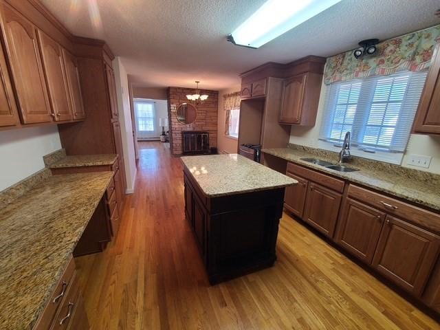 kitchen with light wood-type flooring, a sink, a kitchen island, a textured ceiling, and a brick fireplace