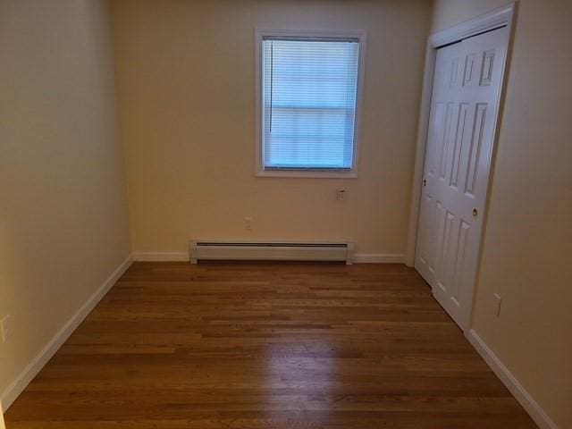 unfurnished bedroom featuring a baseboard heating unit, baseboards, a closet, and wood finished floors