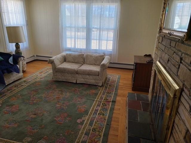 living room featuring baseboard heating, a stone fireplace, and wood finished floors