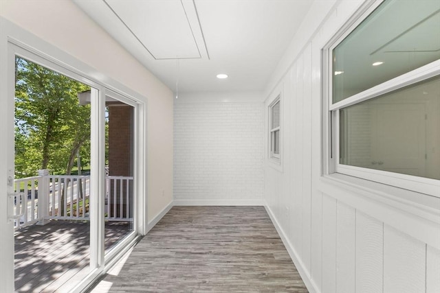 hallway with attic access, wood finished floors, brick wall, and baseboards