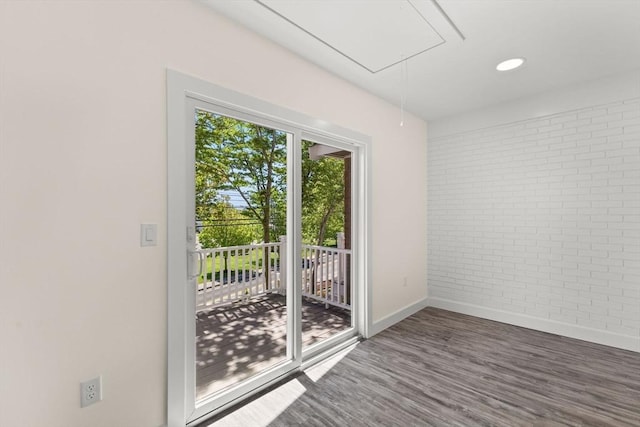 spare room with brick wall, attic access, baseboards, and wood finished floors
