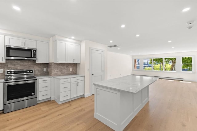kitchen featuring appliances with stainless steel finishes, backsplash, light wood-type flooring, white cabinets, and a center island