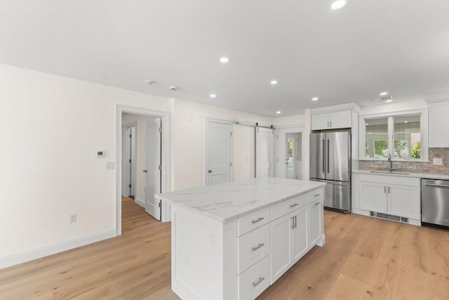 kitchen featuring appliances with stainless steel finishes, a sink, recessed lighting, light wood finished floors, and a center island