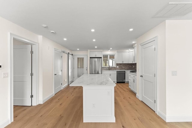 kitchen with appliances with stainless steel finishes, a kitchen island, white cabinetry, light wood-style floors, and recessed lighting