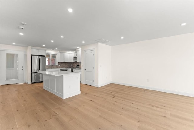 kitchen featuring appliances with stainless steel finishes, light wood finished floors, a kitchen island, baseboards, and recessed lighting