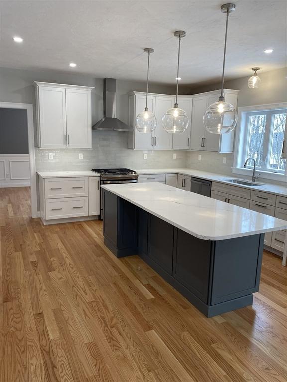 kitchen with light wood-style floors, stainless steel gas stove, a sink, wall chimney range hood, and dishwasher