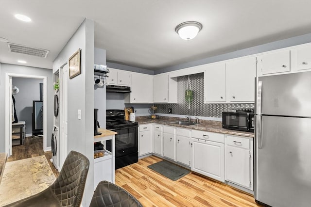221 Oak St Unit 223, Brockton, MA 02302 - kitchen with black appliances, under cabinet range hood, stacked washer / drying machine, light wood finished floors, and white cabinets