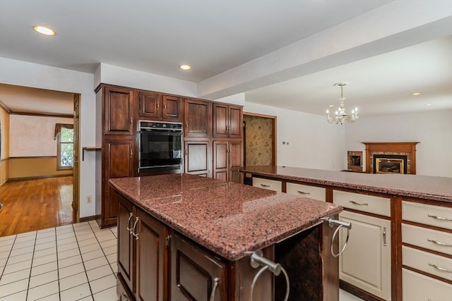 kitchen featuring light tile patterned floors, dark stone counters, a center island, decorative light fixtures, and oven