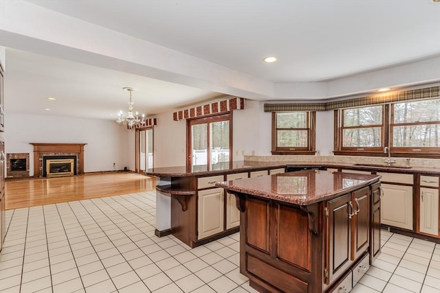 kitchen featuring a fireplace, open floor plan, light tile patterned flooring, a kitchen island, and a sink