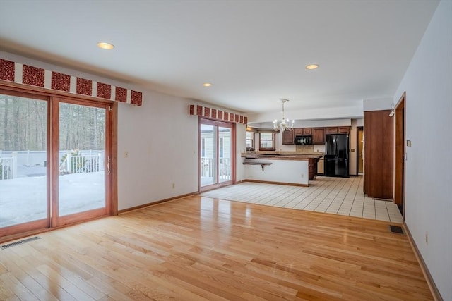 unfurnished living room with baseboards, light wood-style floors, visible vents, and an inviting chandelier