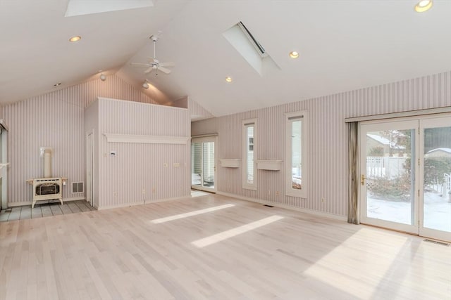 unfurnished living room with a wood stove, light wood-style floors, plenty of natural light, and visible vents