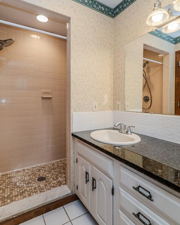 full bath with wallpapered walls, tile patterned flooring, tiled shower, and vanity