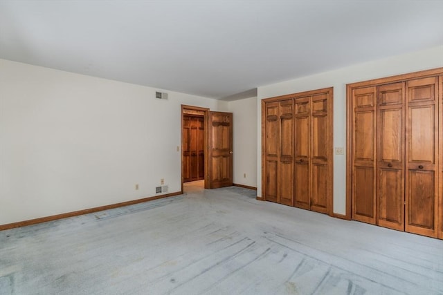 unfurnished bedroom with baseboards, two closets, visible vents, and light colored carpet