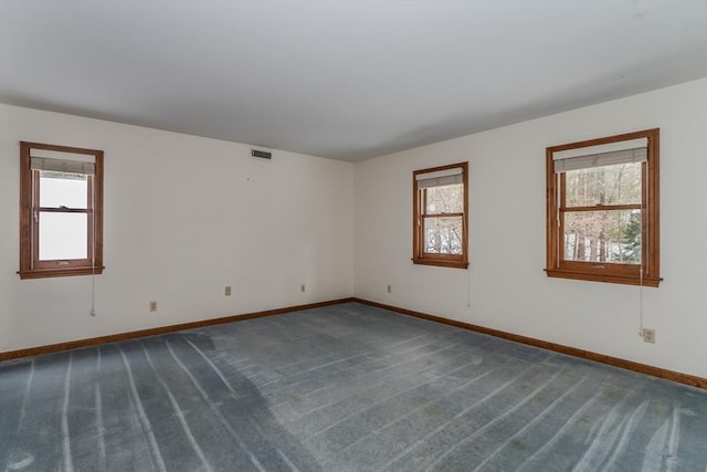 empty room featuring dark colored carpet, visible vents, and baseboards