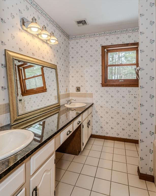 bathroom featuring a sink, visible vents, tile patterned floors, double vanity, and wallpapered walls