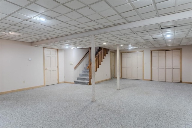 finished below grade area featuring stairway, carpet flooring, a paneled ceiling, and baseboards