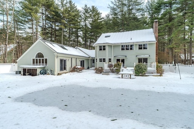 snow covered property with a chimney, central AC unit, and a wooden deck