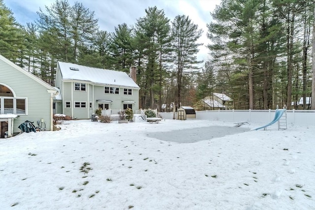 snow covered property featuring a fenced backyard, a chimney, and an outbuilding