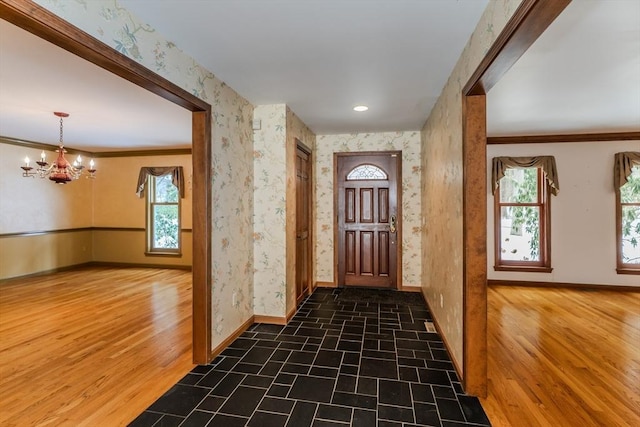 entrance foyer with wallpapered walls, baseboards, a chandelier, and wood finished floors