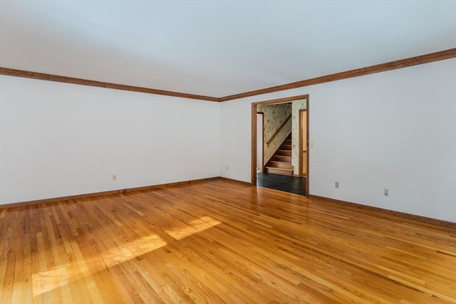 spare room featuring light wood finished floors, baseboards, stairway, and ornamental molding