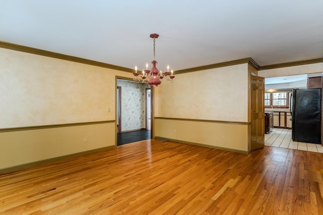 spare room with light wood finished floors, baseboards, a chandelier, and crown molding