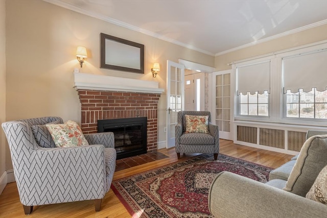 living area with hardwood / wood-style flooring, ornamental molding, and a brick fireplace