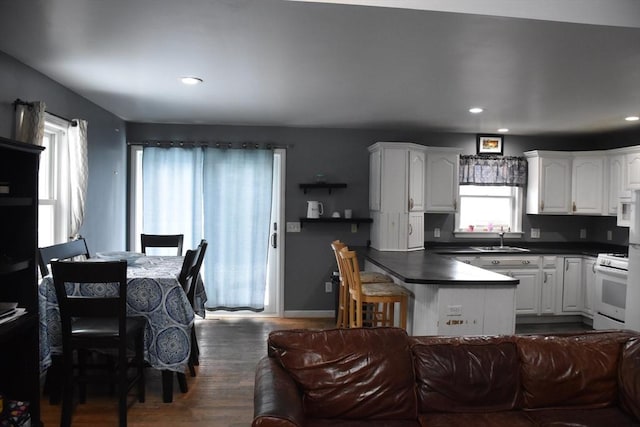 kitchen featuring sink, white gas stove, a breakfast bar area, dark hardwood / wood-style floors, and white cabinets