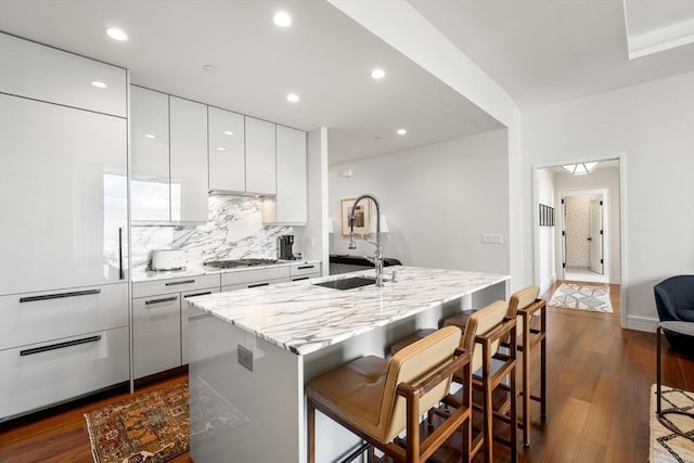 kitchen with stainless steel gas stovetop, dark hardwood / wood-style floors, sink, white cabinetry, and an island with sink