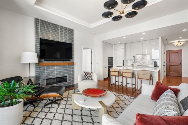 living room featuring light wood-type flooring, a tiled fireplace, and a raised ceiling