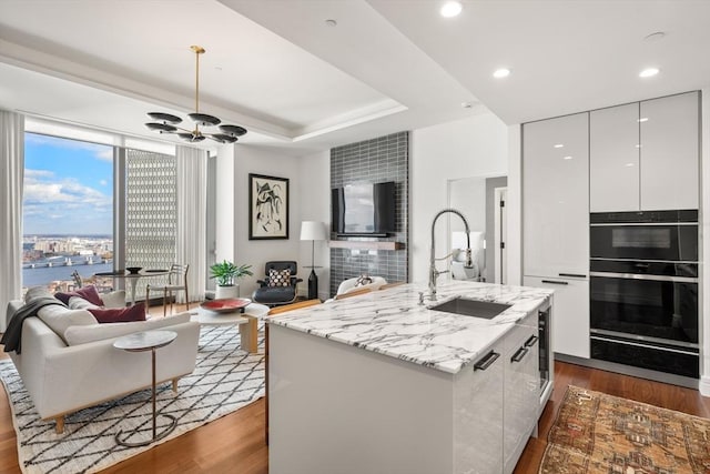 kitchen featuring white cabinetry, dark hardwood / wood-style flooring, sink, a kitchen island with sink, and a water view