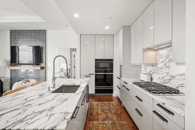 kitchen with stainless steel gas stovetop, backsplash, white cabinets, light stone counters, and sink