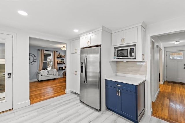 kitchen with appliances with stainless steel finishes, blue cabinets, white cabinetry, backsplash, and light hardwood / wood-style flooring