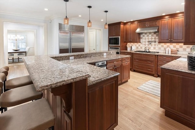 kitchen with built in appliances, light stone counters, decorative light fixtures, a kitchen bar, and a large island