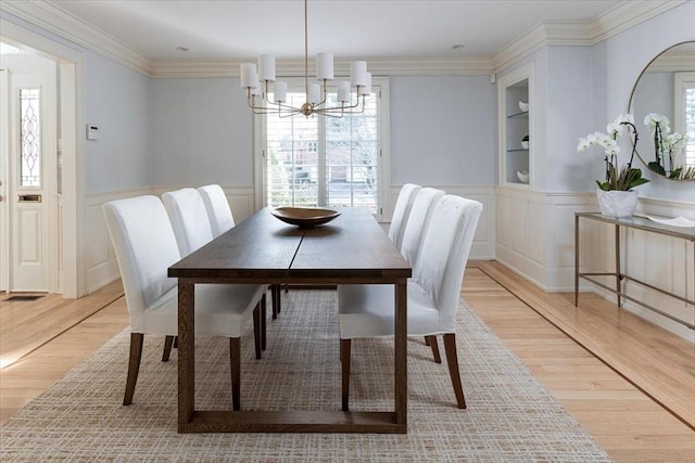 dining space with ornamental molding, light hardwood / wood-style flooring, an inviting chandelier, and built in features