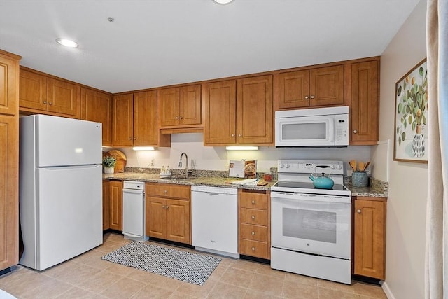 kitchen featuring white appliances, light stone countertops, and sink