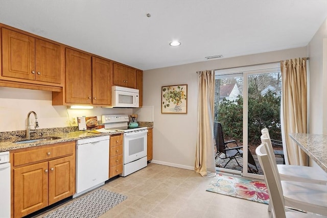 kitchen with white appliances, light stone countertops, and sink