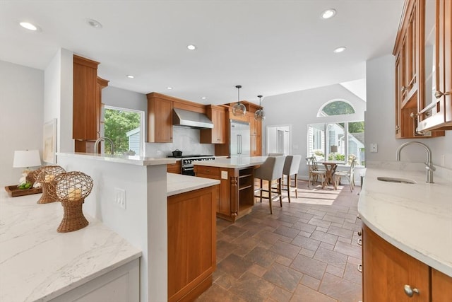 kitchen featuring decorative light fixtures, wall chimney exhaust hood, a breakfast bar area, a kitchen island, and high end stainless steel range