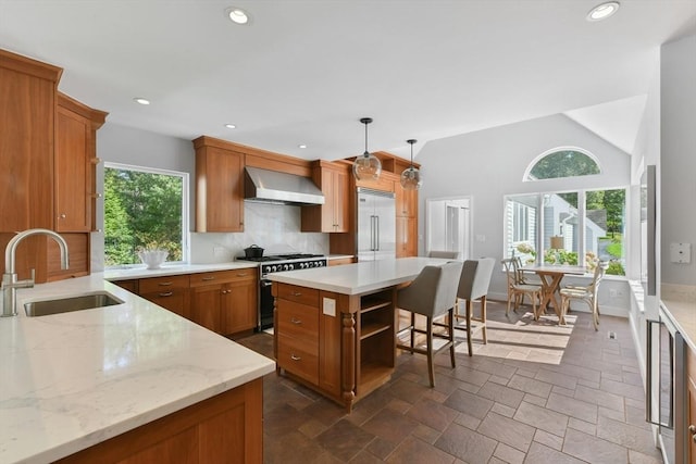 kitchen with hanging light fixtures, a kitchen island, wall chimney exhaust hood, sink, and premium appliances