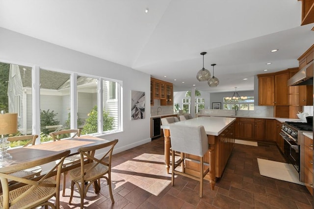 kitchen featuring decorative light fixtures, a center island, wall chimney exhaust hood, high end stainless steel range oven, and a breakfast bar area