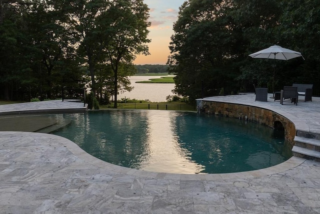 pool at dusk with a patio, pool water feature, and a water view