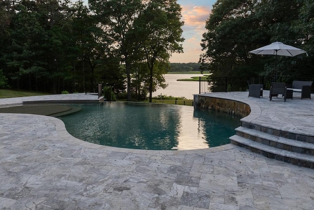 pool at dusk featuring a patio and a water view