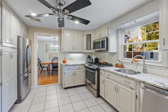 kitchen with white cabinetry, sink, stainless steel appliances, backsplash, and ceiling fan with notable chandelier