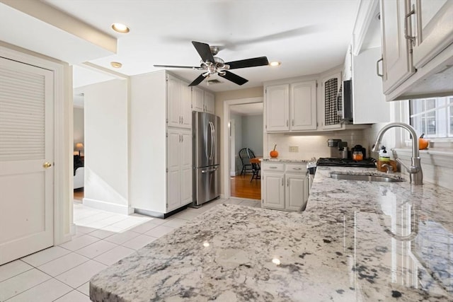 kitchen with white cabinets, sink, ceiling fan, light tile patterned floors, and stainless steel refrigerator