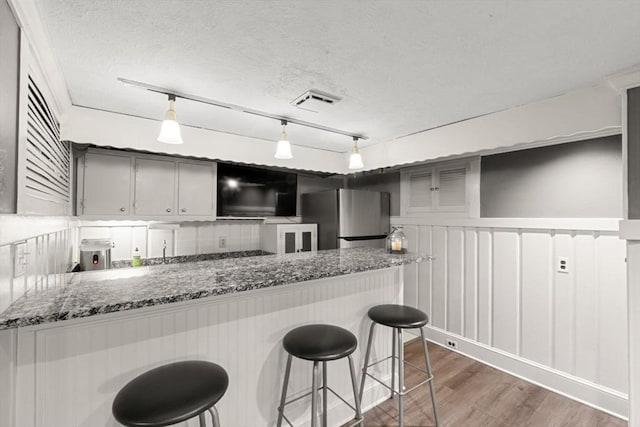 kitchen featuring kitchen peninsula, stainless steel fridge, rail lighting, a textured ceiling, and hanging light fixtures