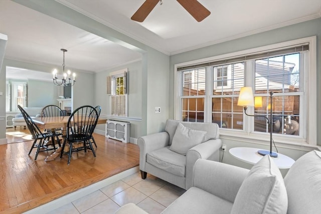 living room with ceiling fan with notable chandelier, a healthy amount of sunlight, light tile patterned floors, and crown molding