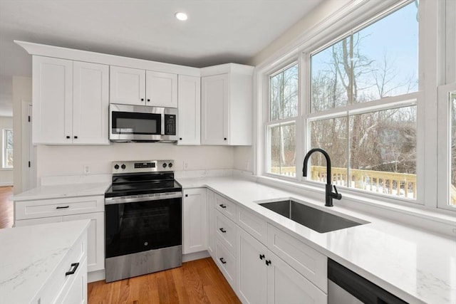 kitchen with appliances with stainless steel finishes, white cabinetry, a sink, and light stone countertops