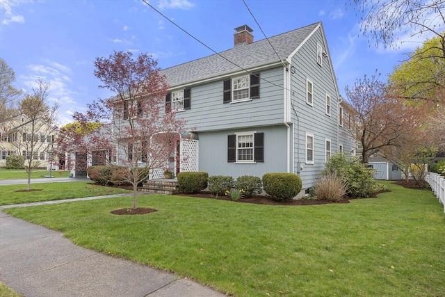colonial inspired home with a front lawn, driveway, a shingled roof, and a chimney