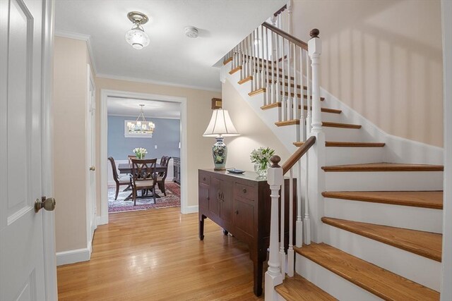 staircase featuring a chandelier, baseboards, wood finished floors, and crown molding