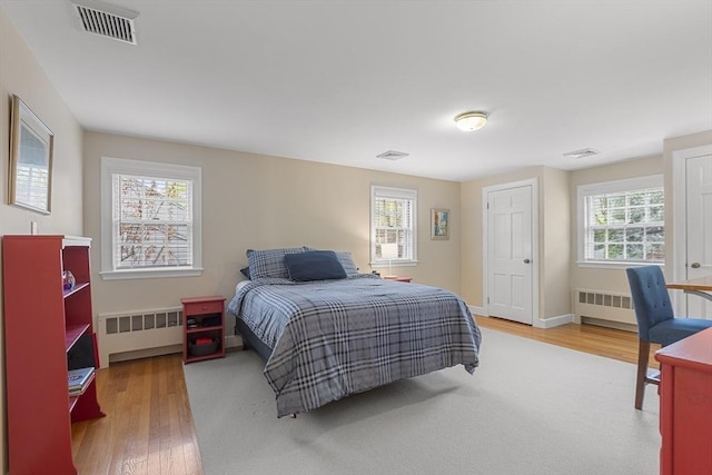bedroom with radiator, visible vents, and wood finished floors