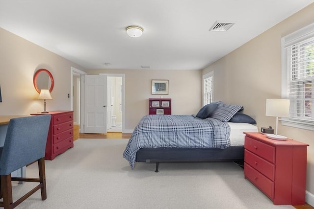 bedroom with visible vents, baseboards, light carpet, and ensuite bathroom